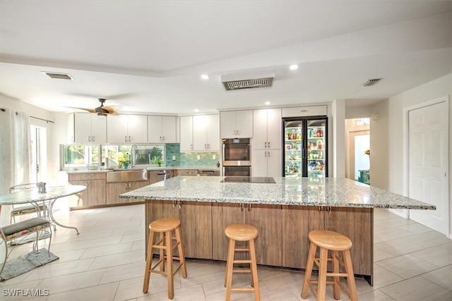 kitchen featuring a large island, white cabinets, decorative backsplash, and sink