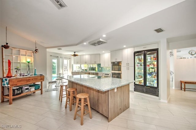 kitchen with white cabinets, a large island, light stone counters, ceiling fan, and tasteful backsplash