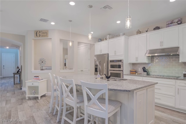 kitchen with decorative light fixtures, tasteful backsplash, stainless steel appliances, and a center island with sink