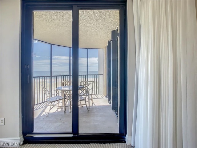 doorway to outside featuring a water view, a beach view, and a textured ceiling