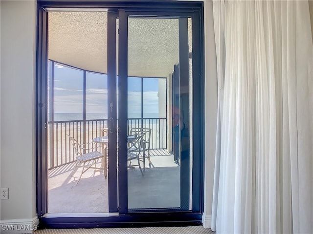 doorway with expansive windows, a water view, and a textured ceiling