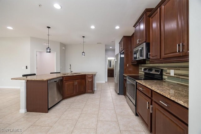 kitchen with a center island with sink, stainless steel appliances, hanging light fixtures, light stone countertops, and sink