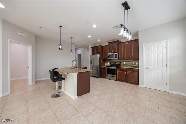 kitchen with a center island with sink, appliances with stainless steel finishes, hanging light fixtures, a breakfast bar, and sink