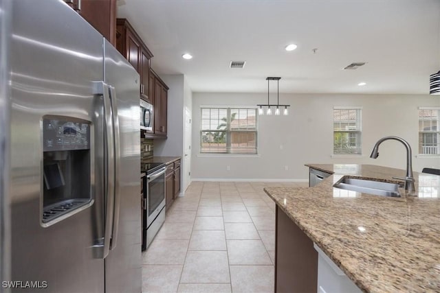 kitchen featuring sink, light stone counters, a wealth of natural light, hanging light fixtures, and appliances with stainless steel finishes