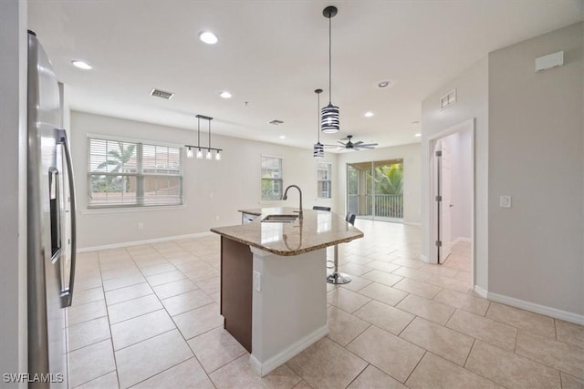 kitchen featuring light stone counters, hanging light fixtures, an island with sink, ceiling fan, and sink