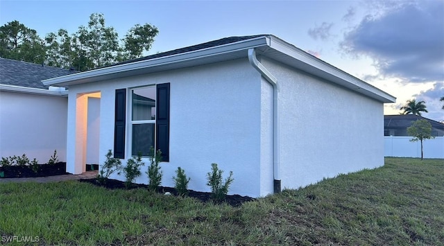 view of home's exterior featuring roof with shingles, a yard, fence, and stucco siding