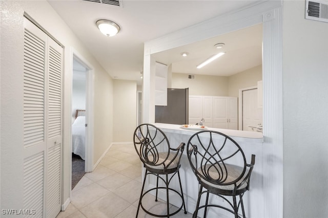 kitchen featuring white cabinetry, a kitchen breakfast bar, kitchen peninsula, stainless steel refrigerator, and light tile patterned floors