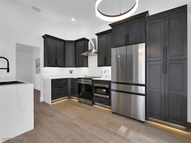 kitchen with sink, light hardwood / wood-style flooring, stainless steel appliances, and wall chimney exhaust hood