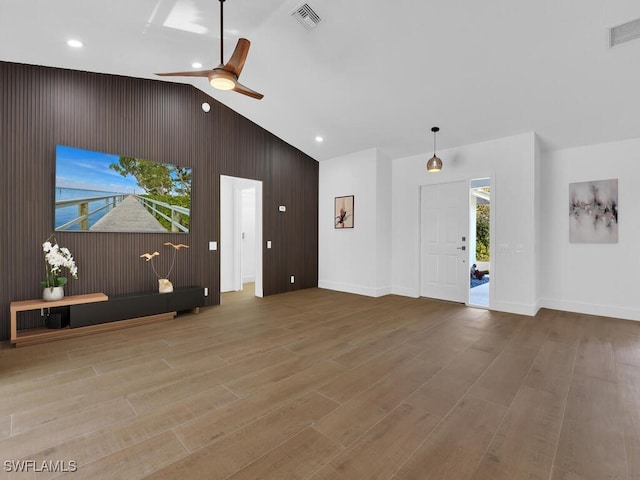 unfurnished living room featuring ceiling fan, wooden walls, high vaulted ceiling, and light wood-type flooring