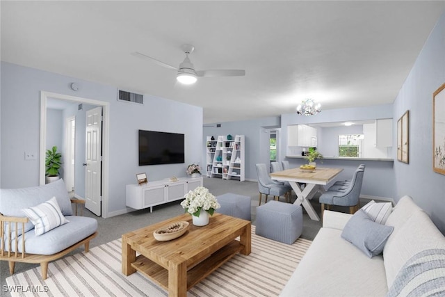 carpeted living room featuring ceiling fan with notable chandelier