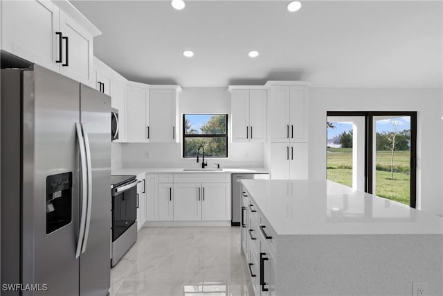 kitchen featuring appliances with stainless steel finishes, white cabinetry, a kitchen island, and sink