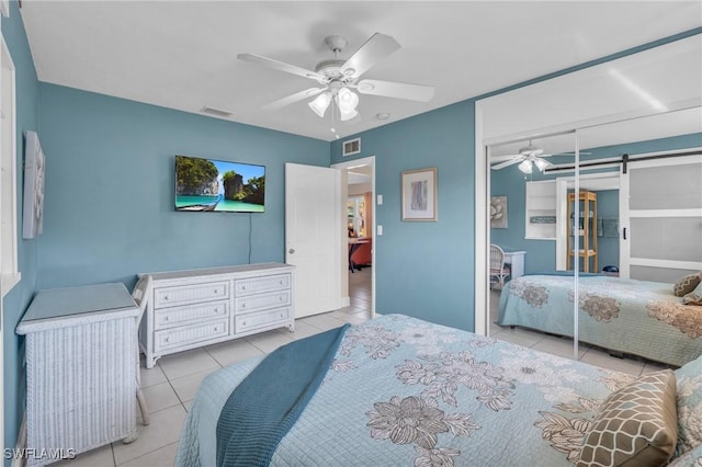 tiled bedroom featuring ceiling fan, a barn door, and a closet