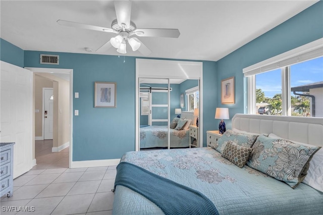 bedroom featuring ceiling fan, a barn door, light tile patterned flooring, and a closet