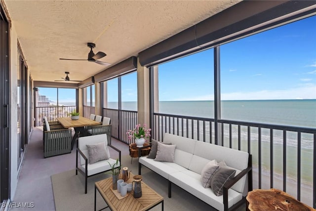 sunroom with a water view, ceiling fan, and a beach view