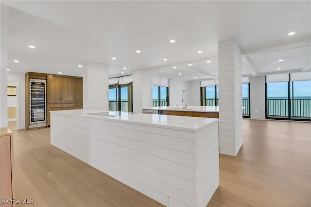 kitchen featuring sink, decorative columns, wine cooler, a large island with sink, and light wood-type flooring