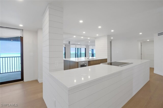 kitchen with a spacious island, black electric stovetop, sink, and light wood-type flooring