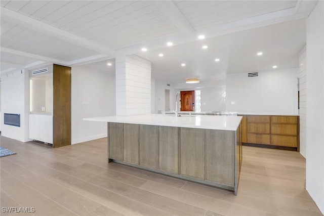 kitchen with a sink, light countertops, a large island, light wood-type flooring, and beamed ceiling