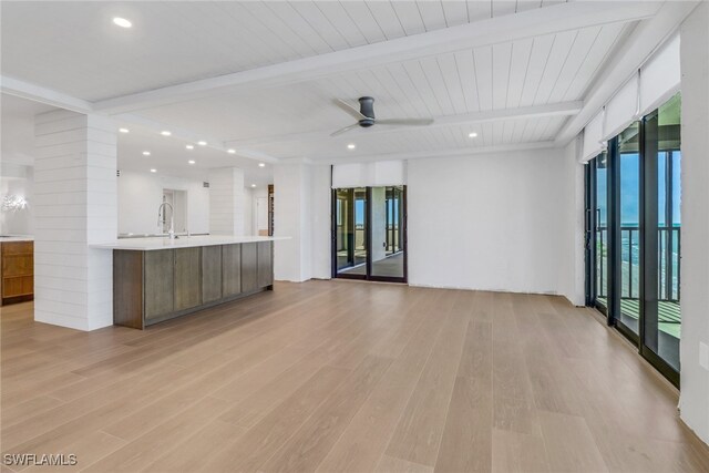 unfurnished living room featuring beam ceiling, a wealth of natural light, light hardwood / wood-style floors, and ceiling fan