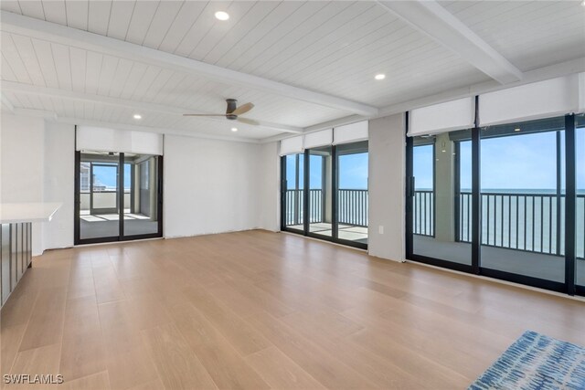 spare room with ceiling fan, light hardwood / wood-style floors, floor to ceiling windows, a water view, and beam ceiling