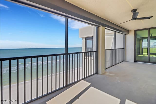 balcony featuring a water view, ceiling fan, and a beach view