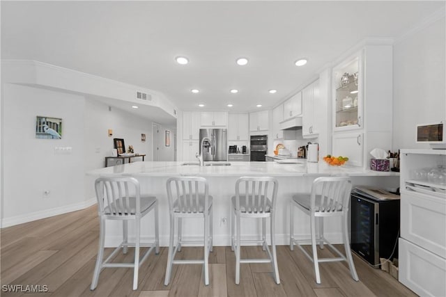 kitchen featuring a kitchen breakfast bar, kitchen peninsula, wine cooler, appliances with stainless steel finishes, and white cabinetry