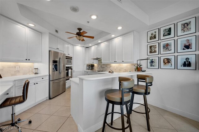 kitchen with a kitchen breakfast bar, white cabinetry, a tray ceiling, and stainless steel appliances