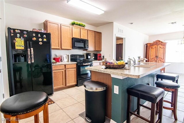 kitchen featuring a breakfast bar, sink, a kitchen island with sink, light tile patterned floors, and black appliances