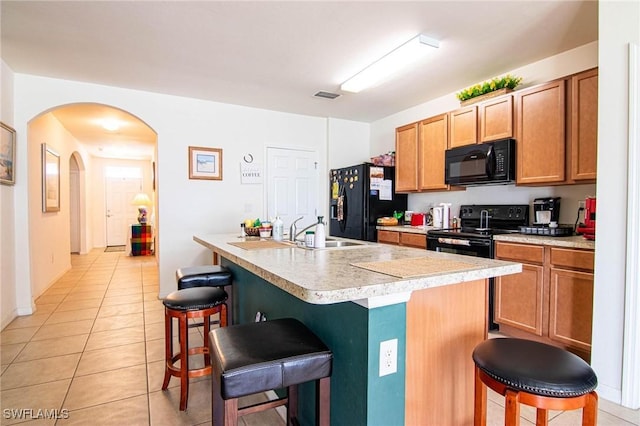 kitchen with sink, a kitchen breakfast bar, a kitchen island with sink, light tile patterned floors, and black appliances