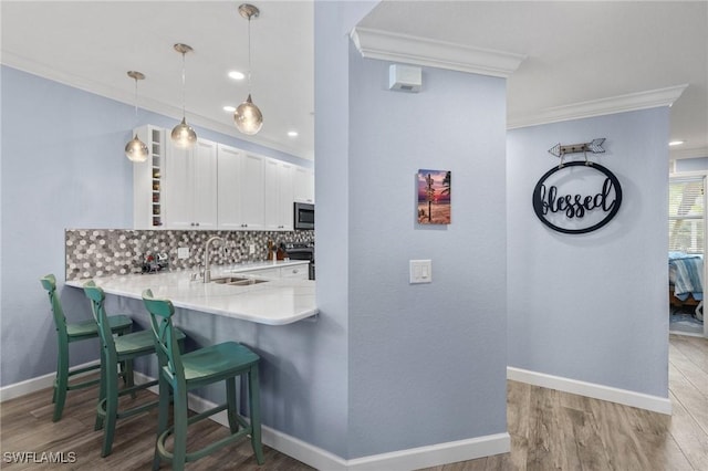 kitchen with kitchen peninsula, backsplash, crown molding, sink, and white cabinetry