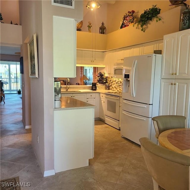 kitchen with white appliances, backsplash, a high ceiling, white cabinets, and sink