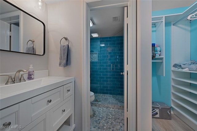 bathroom with hardwood / wood-style floors, toilet, vanity, and a tile shower