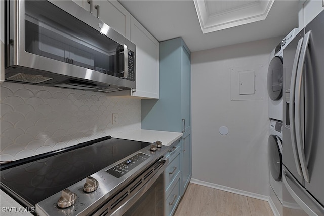 kitchen with white cabinets, appliances with stainless steel finishes, stacked washer and dryer, light hardwood / wood-style floors, and crown molding