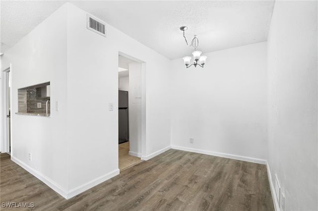 unfurnished dining area featuring dark hardwood / wood-style flooring, a textured ceiling, and a chandelier