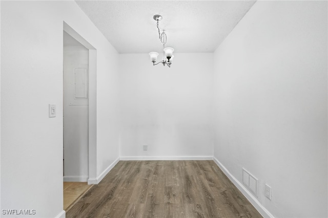 unfurnished dining area with a textured ceiling, hardwood / wood-style floors, and a notable chandelier