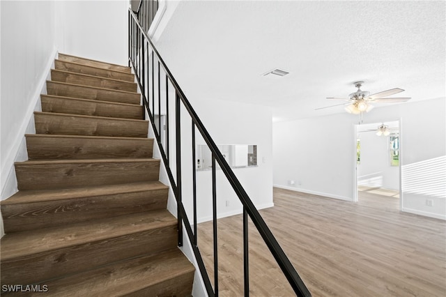 stairway with hardwood / wood-style flooring, a textured ceiling, and ceiling fan