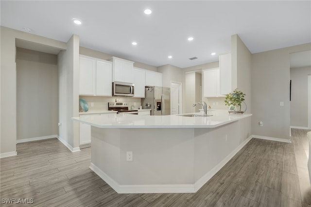 kitchen featuring appliances with stainless steel finishes, white cabinetry, sink, kitchen peninsula, and light wood-type flooring