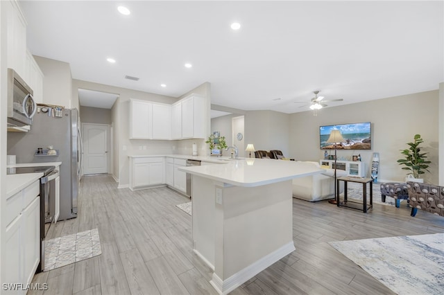 kitchen with stainless steel appliances, kitchen peninsula, light wood-type flooring, and white cabinets