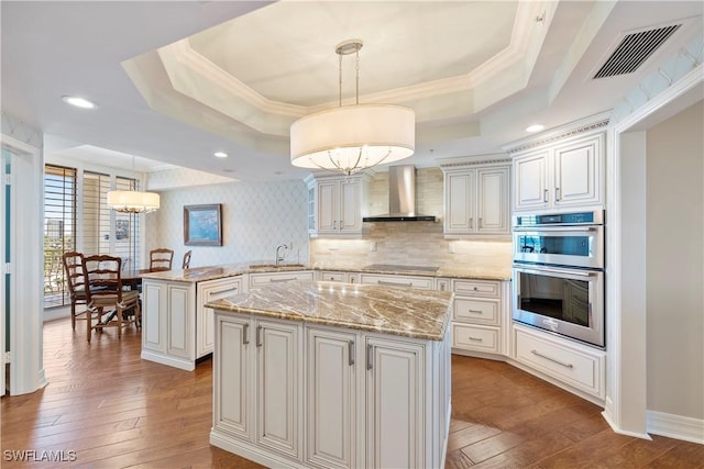 kitchen with a kitchen island, a raised ceiling, wall chimney exhaust hood, and pendant lighting