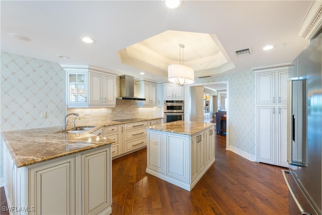 kitchen with sink, wall chimney exhaust hood, hanging light fixtures, a kitchen island, and appliances with stainless steel finishes