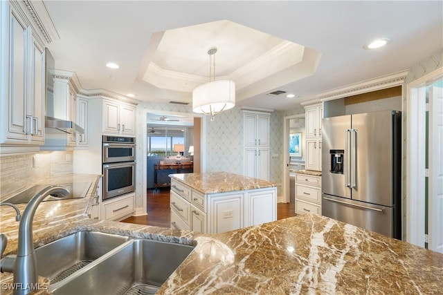 kitchen featuring a raised ceiling, appliances with stainless steel finishes, pendant lighting, light stone counters, and a kitchen island