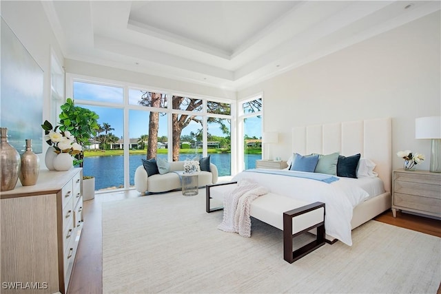 bedroom with access to outside, wood finished floors, a water view, and a raised ceiling