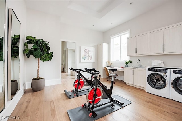 exercise room with baseboards, light wood-style flooring, independent washer and dryer, a tray ceiling, and a sink