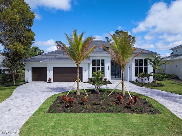 view of front of home with a garage, decorative driveway, a front lawn, and stucco siding