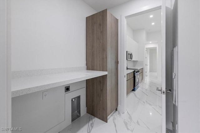 kitchen featuring light stone counters, white cabinetry, stainless steel appliances, and built in desk