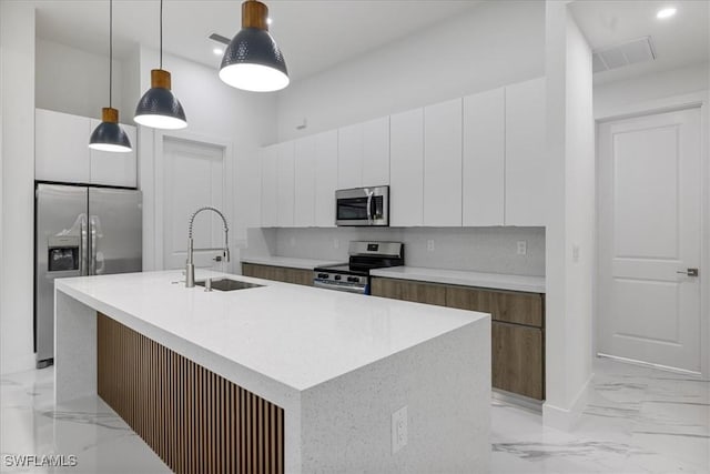 kitchen featuring pendant lighting, white cabinetry, stainless steel appliances, tasteful backsplash, and a center island with sink