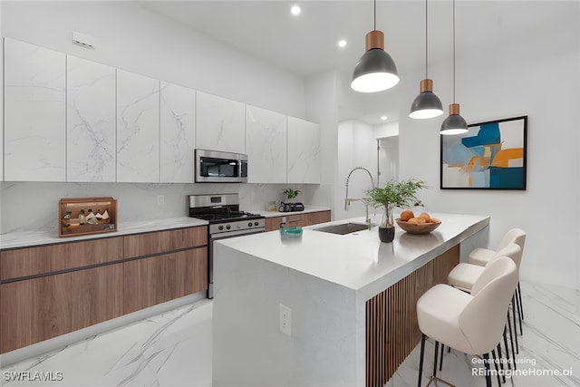 kitchen with a breakfast bar area, appliances with stainless steel finishes, a kitchen island with sink, pendant lighting, and sink