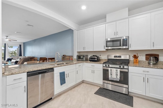 kitchen with ceiling fan, sink, white cabinetry, stainless steel appliances, and light stone counters