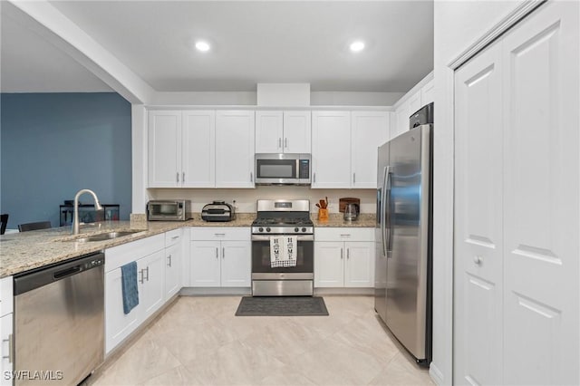 kitchen featuring kitchen peninsula, appliances with stainless steel finishes, light stone countertops, white cabinets, and sink