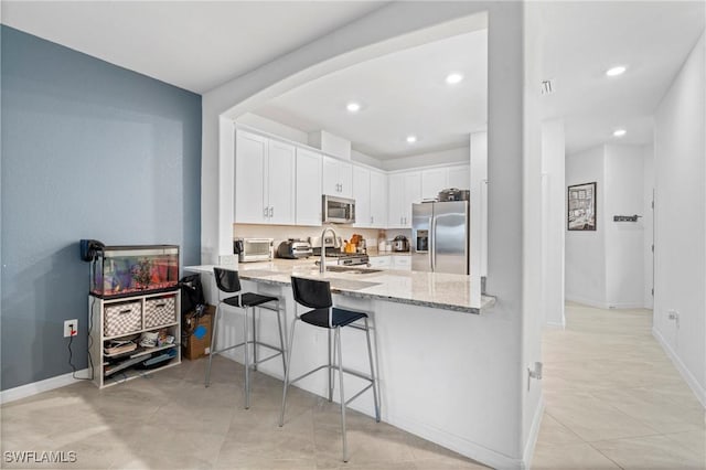 kitchen with appliances with stainless steel finishes, white cabinetry, kitchen peninsula, light stone counters, and a breakfast bar area