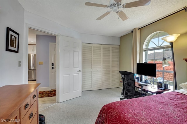 carpeted bedroom with ceiling fan, a closet, stainless steel refrigerator, and a textured ceiling